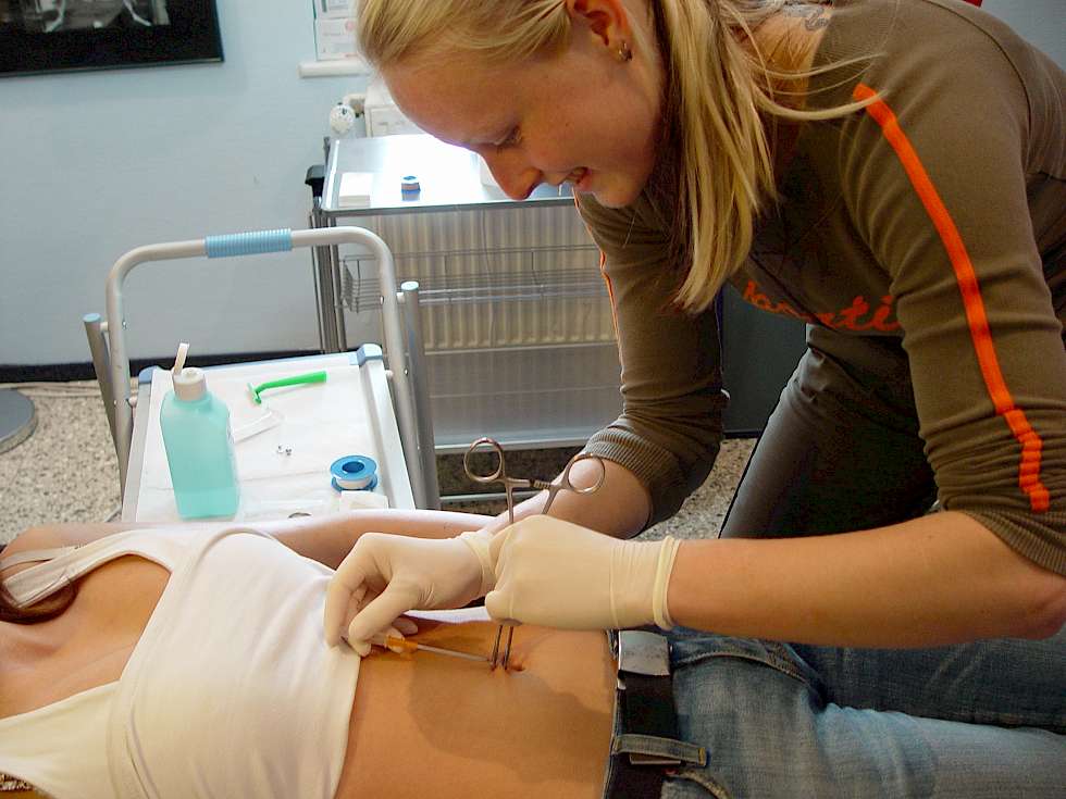 Seminarteilnehmerin Schüerin bei Piercingvorgang Bauchnabel am Model Bild Piercing Seminar